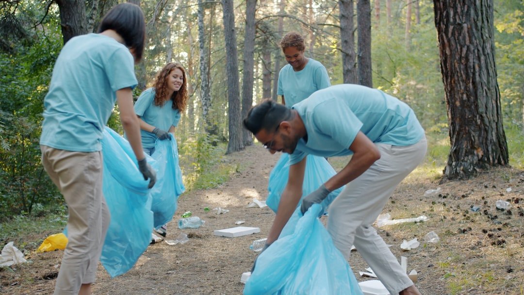 Laughing young people men and women are picking garbage in forest cleaning nature having fun together on summer day. Youth and volunteering concept.